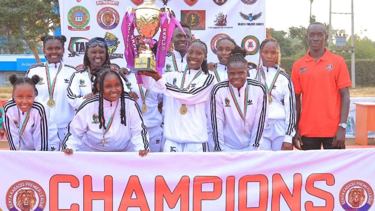 JKUAT Starlets, in white tracksuits, with the KKPL Season 2 trophy behind a “Champions” banner.